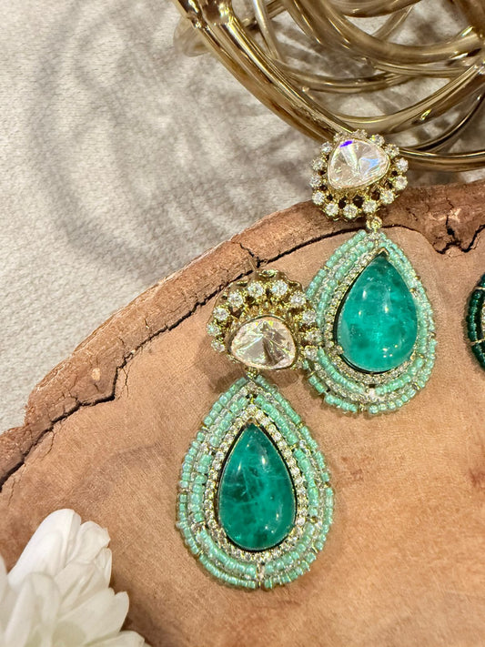 Green teardrop earrings with gold accents on a textured surface