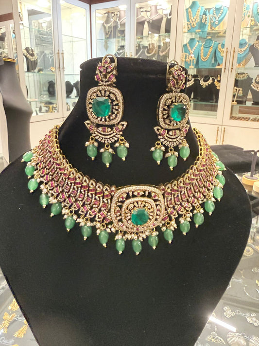 Ornate necklace and earrings set with green stones on a black stand.
