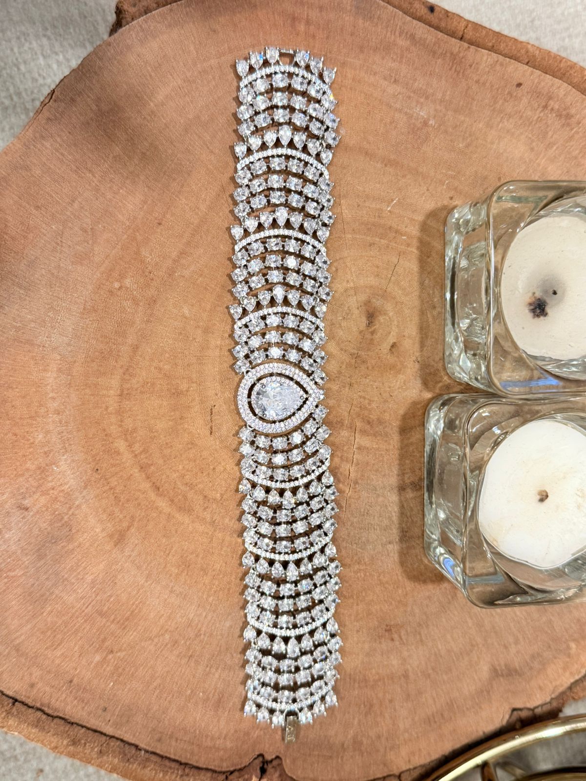 Silver bracelet with multiple rows of diamonds on a wooden surface with candles.