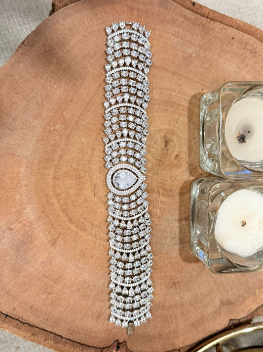 Silver bracelet with multiple rows of diamonds on a wooden surface with candles.