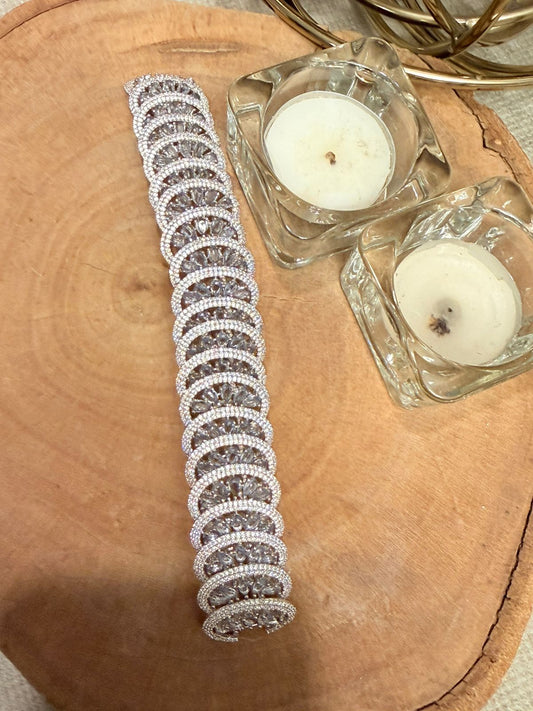 Silver bracelet with crystals on a wooden surface with two small candles.