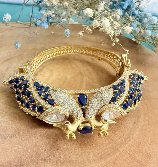 Gold and blue decorative item on a wooden surface with flowers in the background
