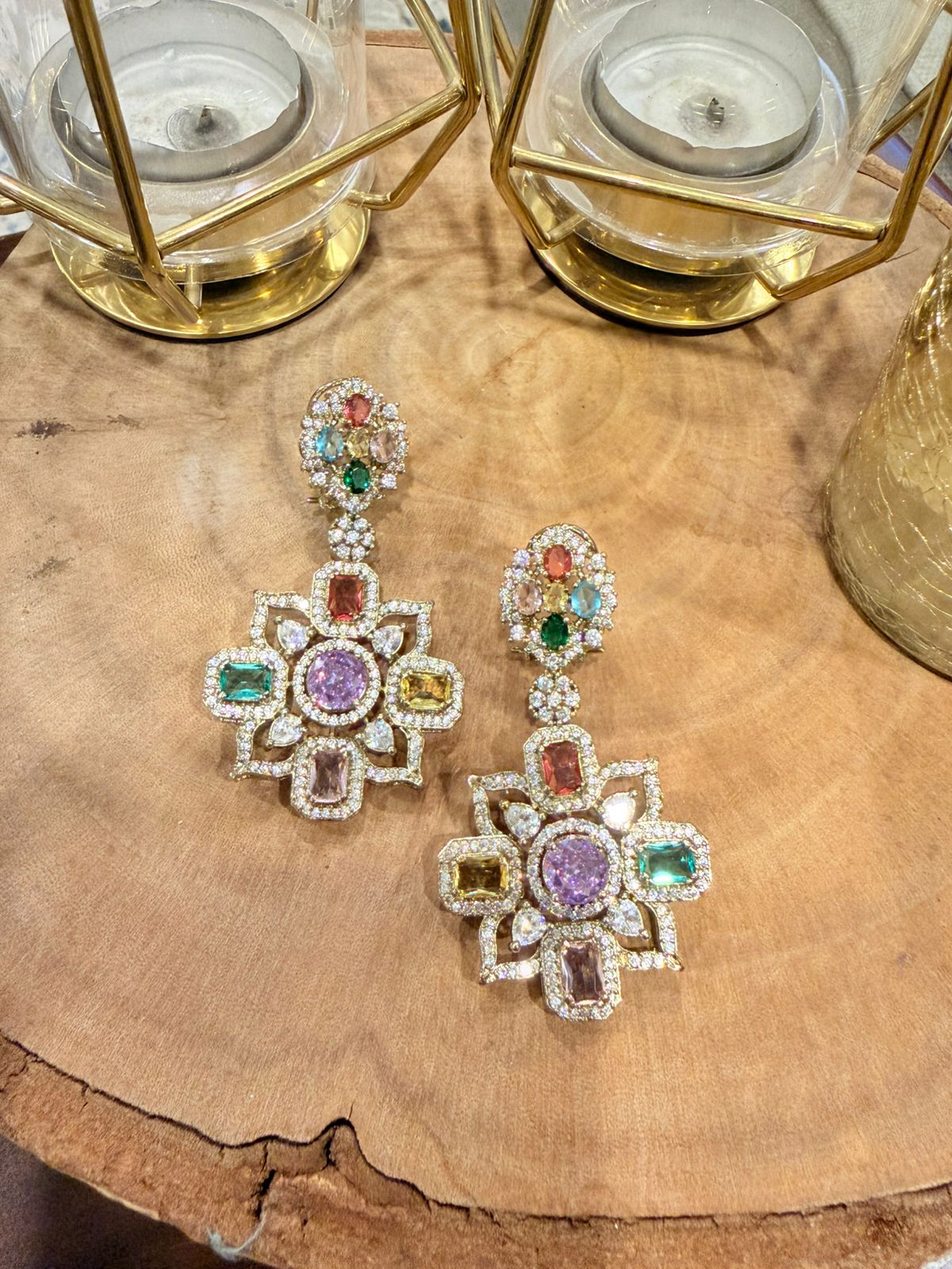 Multicolored gemstone earrings on a wooden surface with candle holders in the background.
