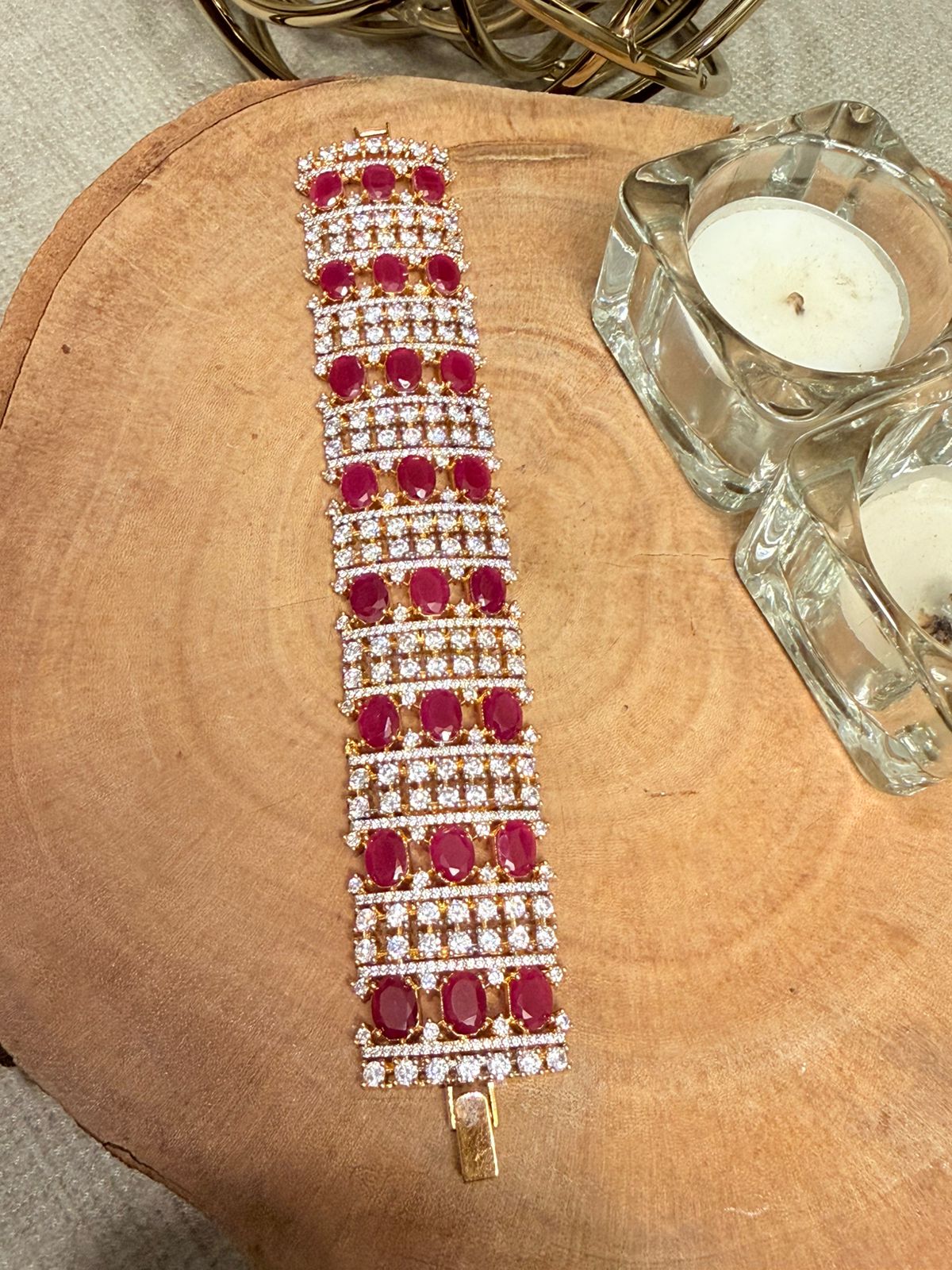 Elegant bracelet with red gemstones and gold accents on a wooden surface.