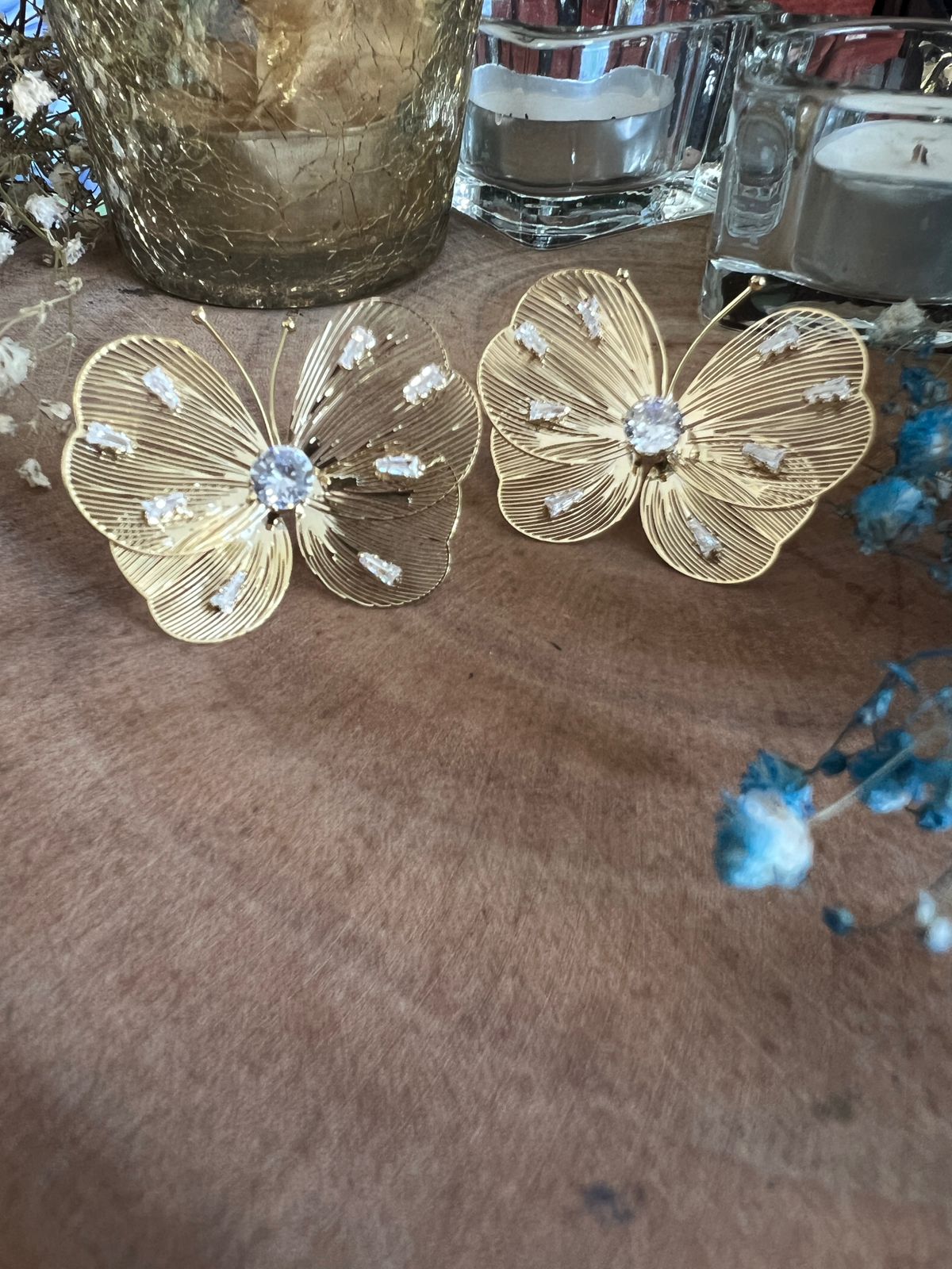 Gold butterfly-shaped earrings with clear stones on a textured surface.