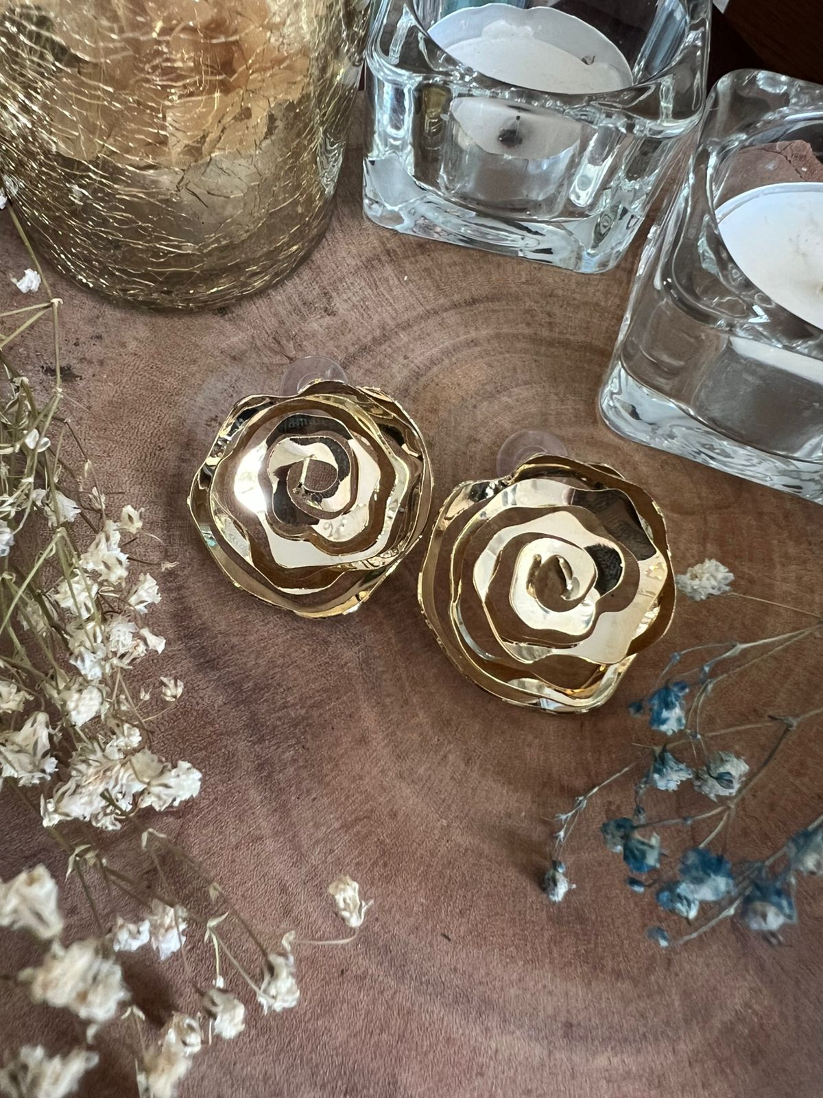 Gold rose-shaped objects on a wooden surface with dried flowers and glass containers.