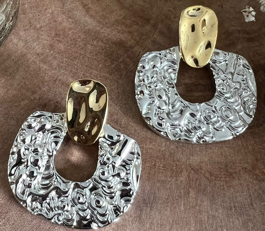 Pair of silver and gold earrings on a brown surface