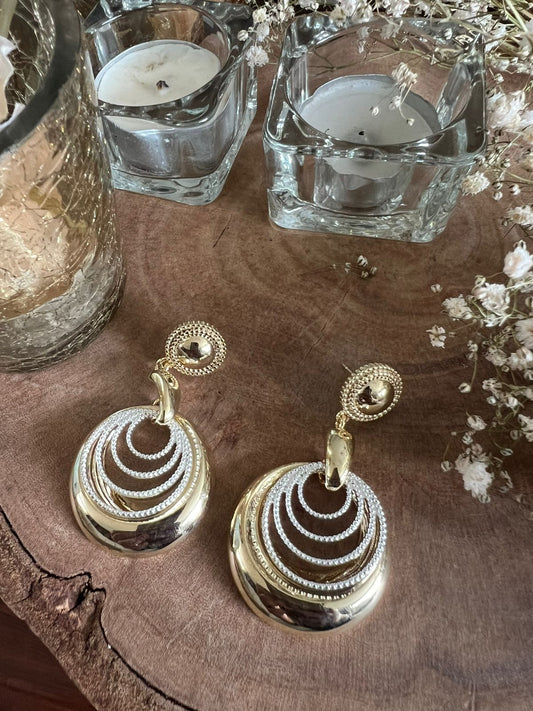 Gold earrings on a wooden surface with candles and flowers in the background