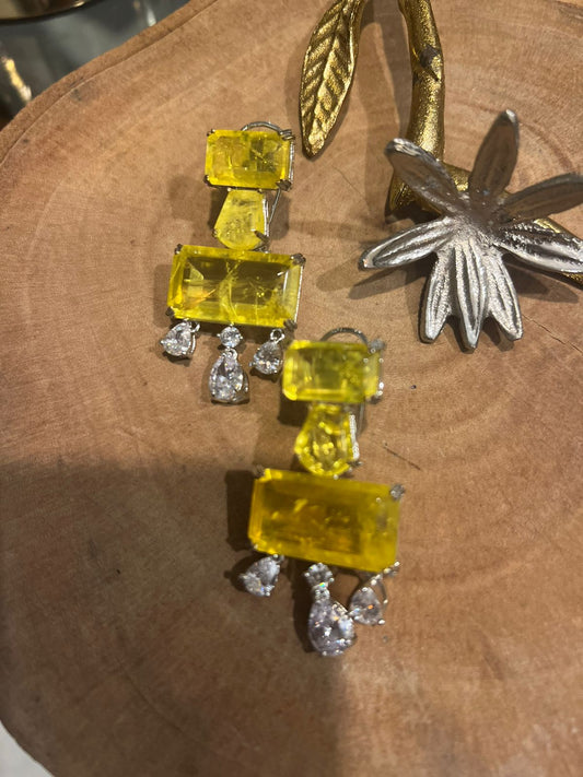 Pair of earrings with yellow gemstones and silver accents on a wooden surface