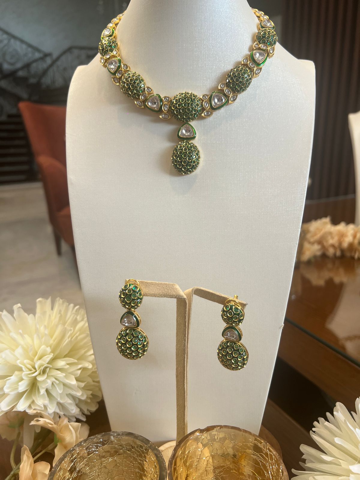 Green and gold necklace and earrings on a mannequin bust with flowers in the foreground.