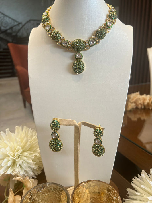 Green and gold necklace and earrings on a mannequin bust with flowers in the foreground.