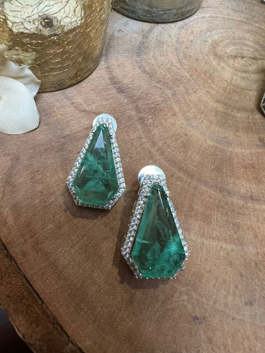 Green gemstone earrings with silver accents on a wooden surface
