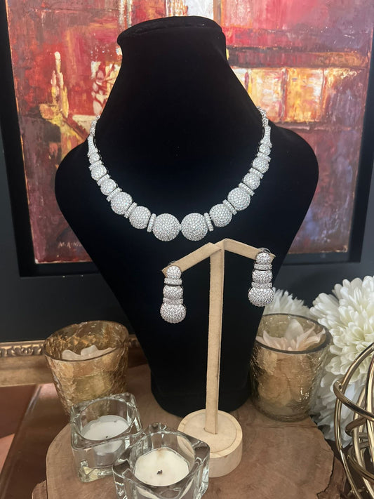Diamond necklace and earrings on a black mannequin with candles and flowers in the background.
