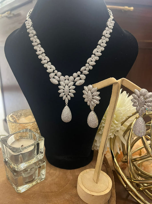 Silver necklace and earrings on a black mannequin with decorative items in the background.