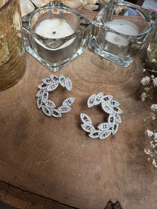 Pair of silver hoop earrings with clear stones on a wooden surface with candles in the background.