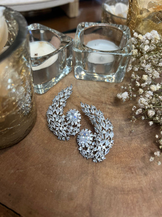 Silver earrings on a wooden surface with candles and flowers in the background