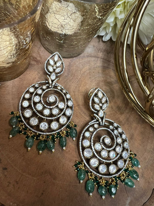 Ornate earrings with green beads on a wooden surface