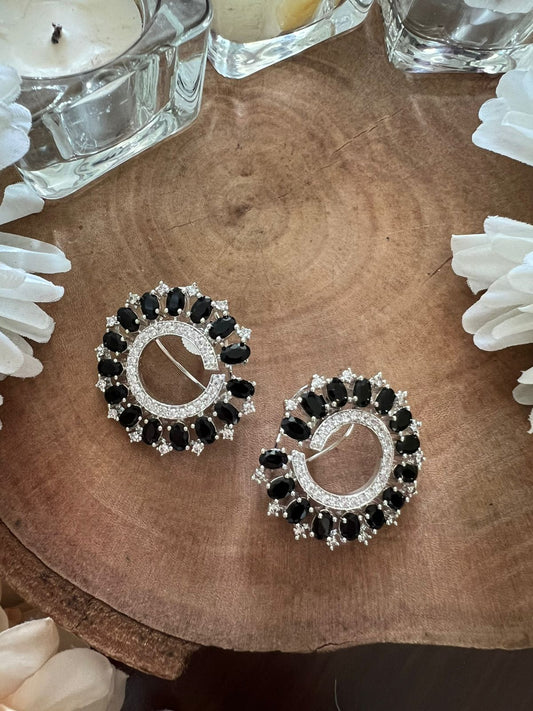 Pair of black and silver hoop earrings on a wooden surface with white flowers and candles.