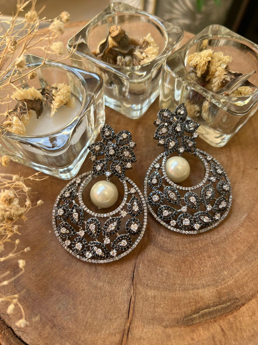 Pair of ornate earrings with pearls on a wooden surface with small glass containers.