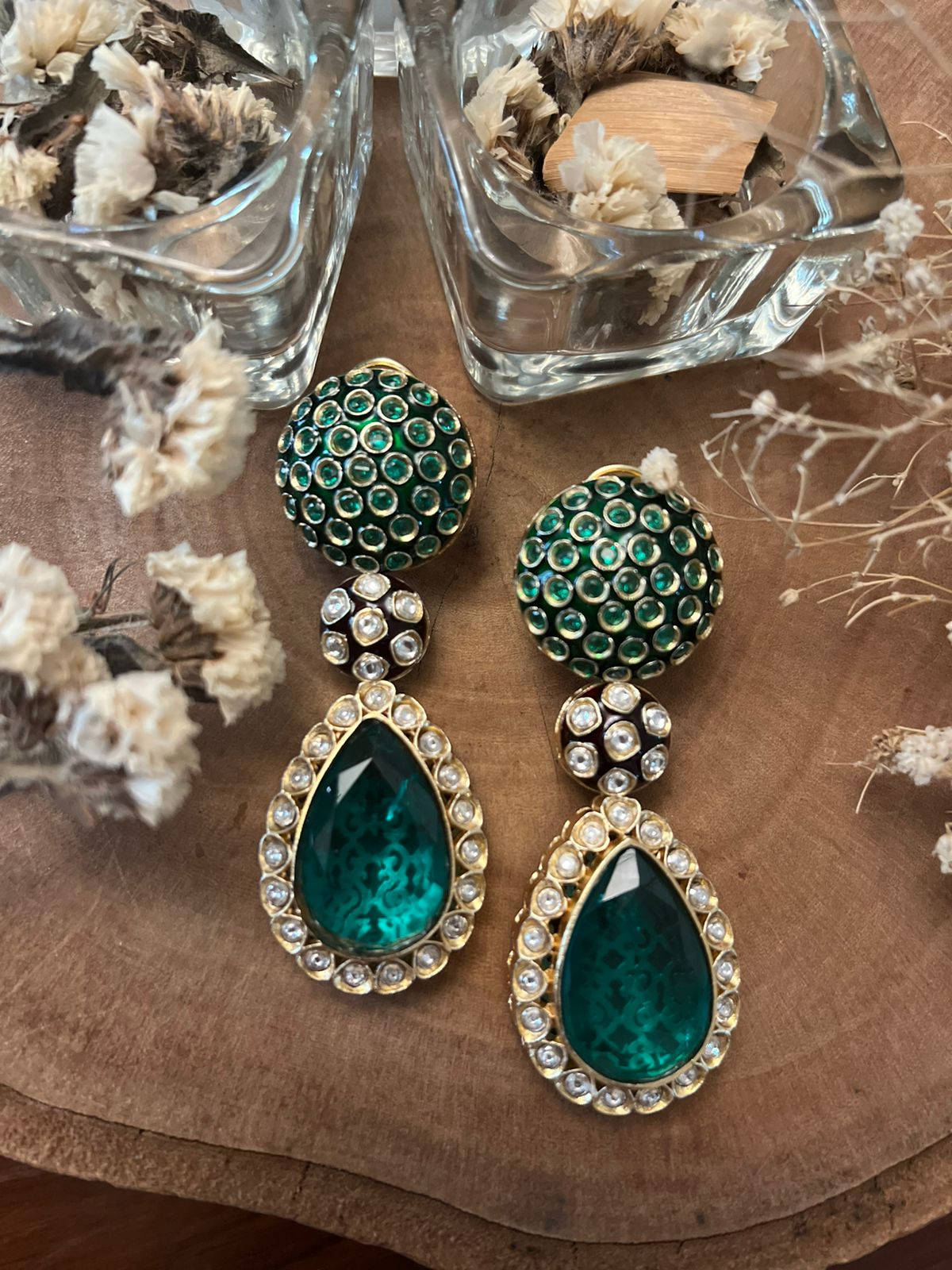 Pair of green teardrop earrings with gold accents on a wooden surface.