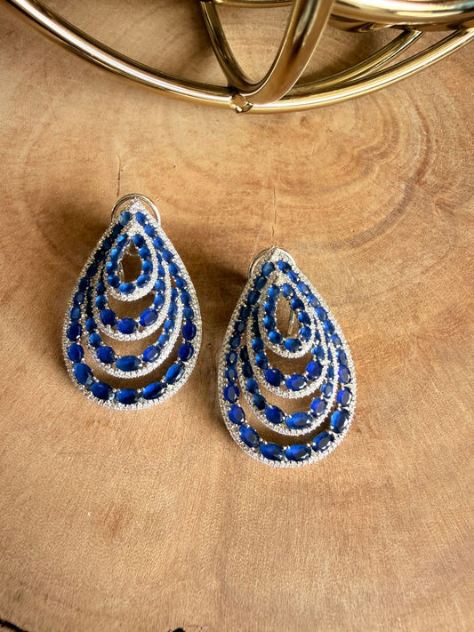 Teardrop-shaped earrings with blue and silver design on a wooden surface