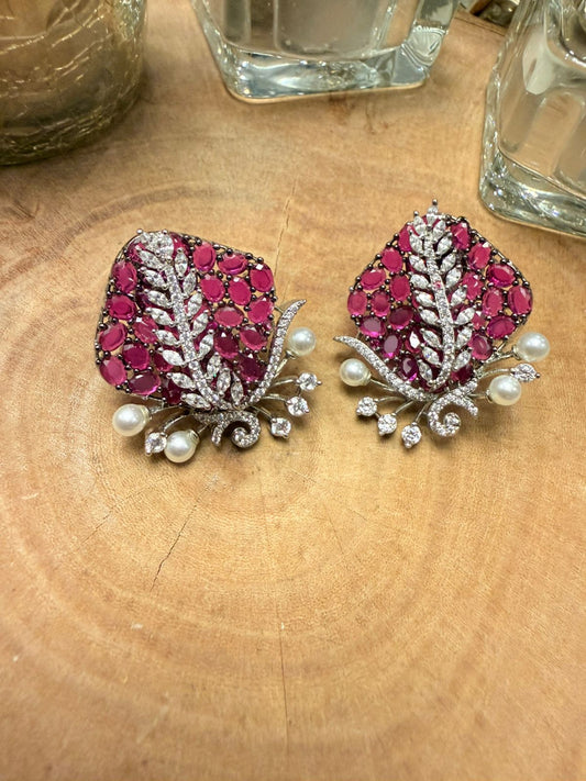 Pair of ornate earrings with pink gemstones and pearl accents on a wooden surface.