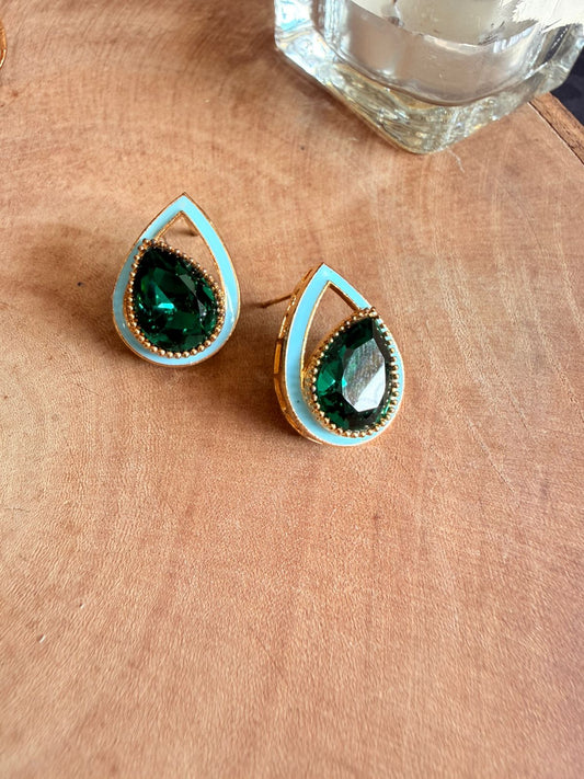 Teardrop-shaped earrings with green gemstones on a beige surface