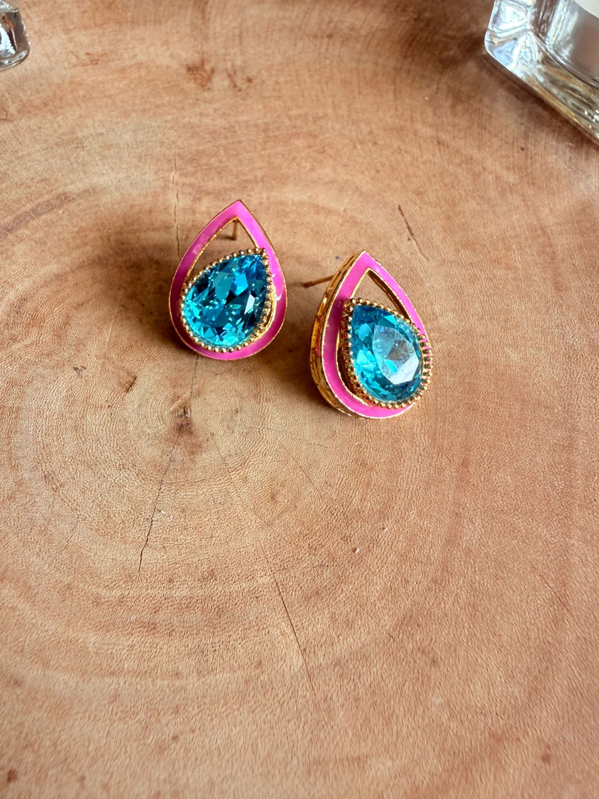 Teardrop-shaped earrings with blue gemstones and pink and gold accents on a wooden surface.