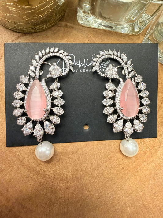 Pair of earrings with pink stones and pearl drops on a black card with 'Sahil by Sehaj' branding, placed on a wooden surface.