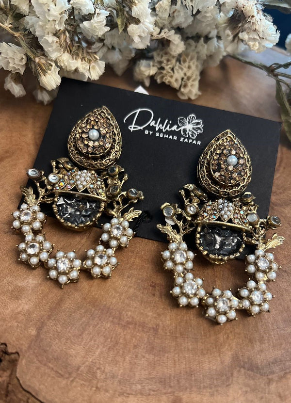 Antique gold earrings with intricate detailing and clustered pearls displayed on a wooden surface.